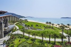 Un resort con vista a la playa, palmeras y jardines cuidados.