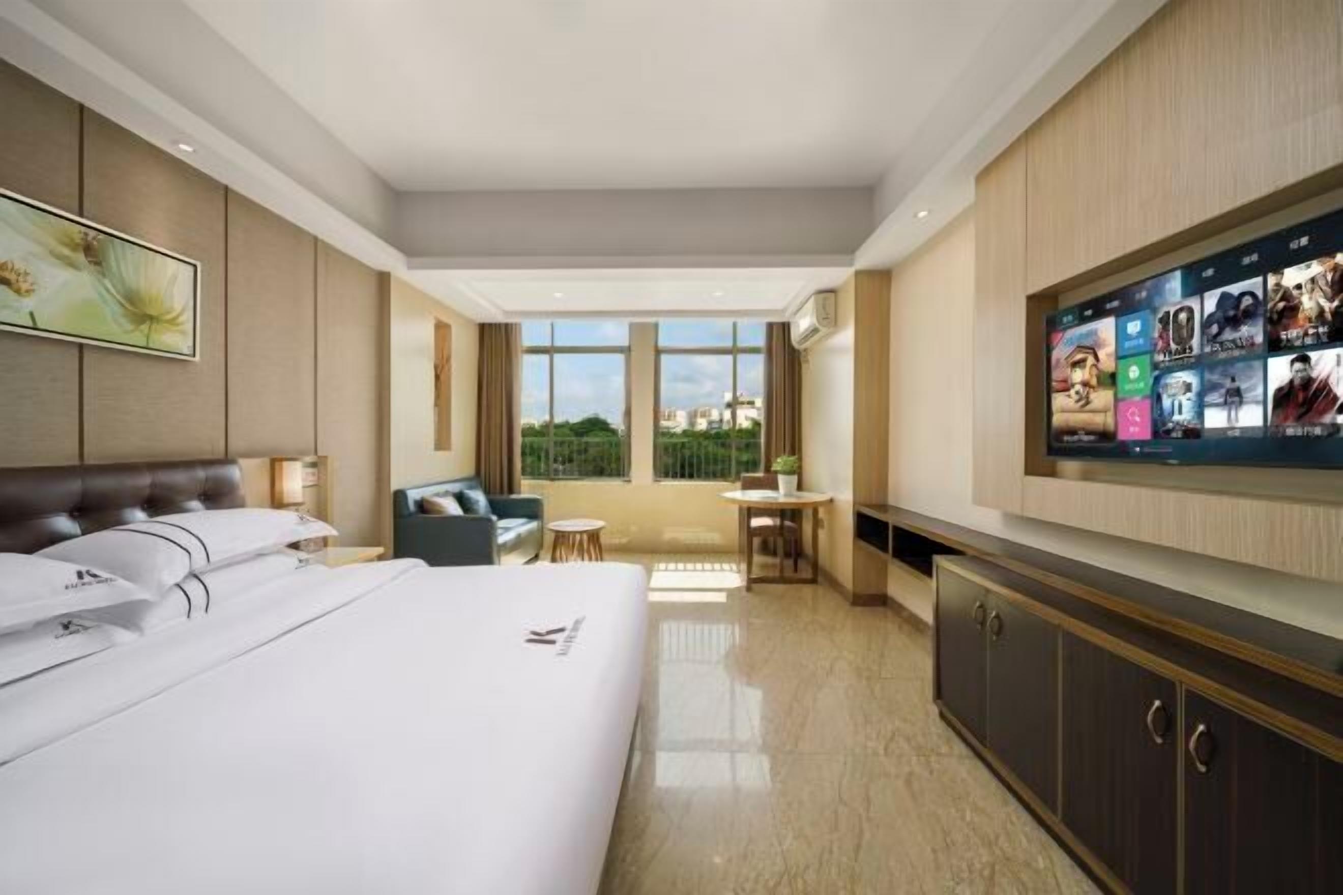 Een hotelkamer met een groot bed, een aan de muur bevestigde televisie, een zithoek met een tafel en stoelen, en uitzicht op het omliggende landschap door grote ramen.