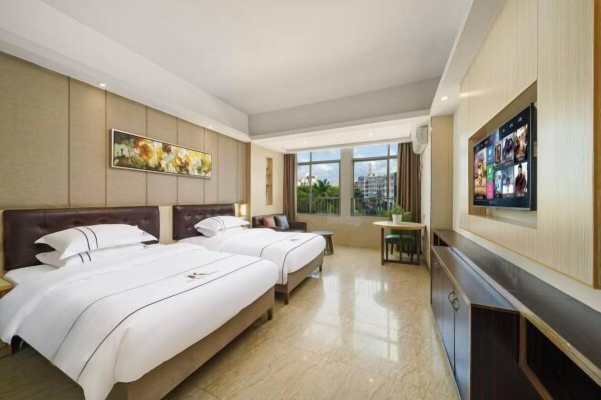 A hotel room with two beds, a TV, a desk, and a large window.