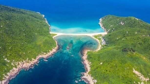An aerial view of a coastal area with a narrow waterway leading to a beach, surrounded by green hills. - Kaiwei Hotel (Wanning High-speed Railway Station Branch) (Wanning)