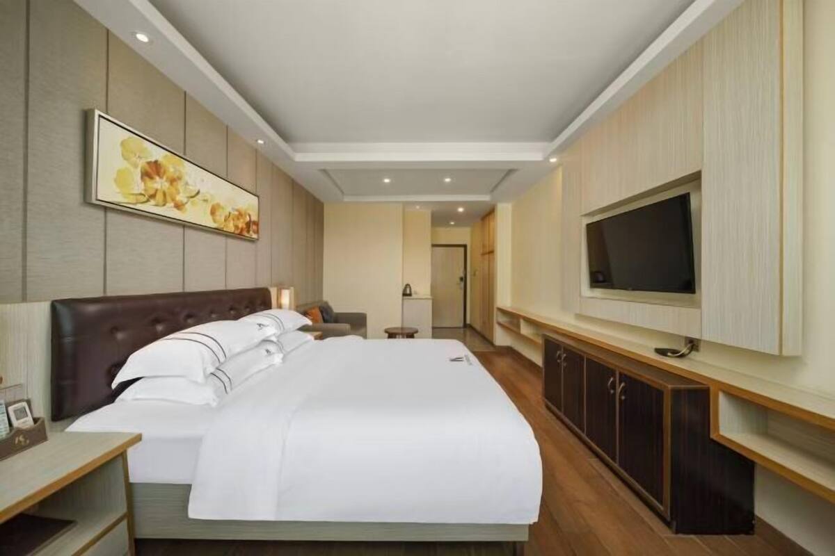 A hotel room with a large bed, a TV mounted on the wall, and a wooden cabinet.