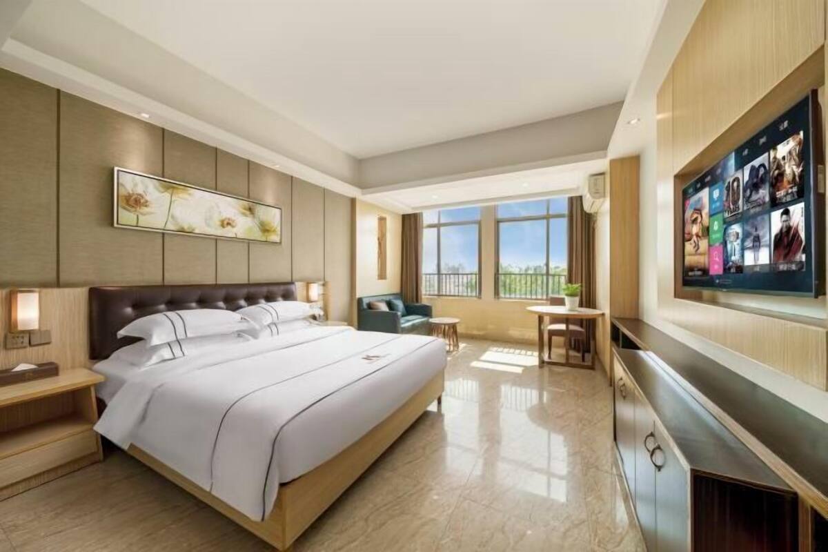 A hotel room with a large bed, a TV mounted on the wall, a desk, and a view of the outdoors.