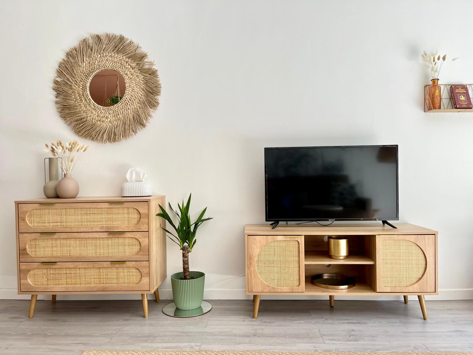 Un salon moderne avec un téléviseur, un meuble en rotin et un grand miroir décoratif au mur.