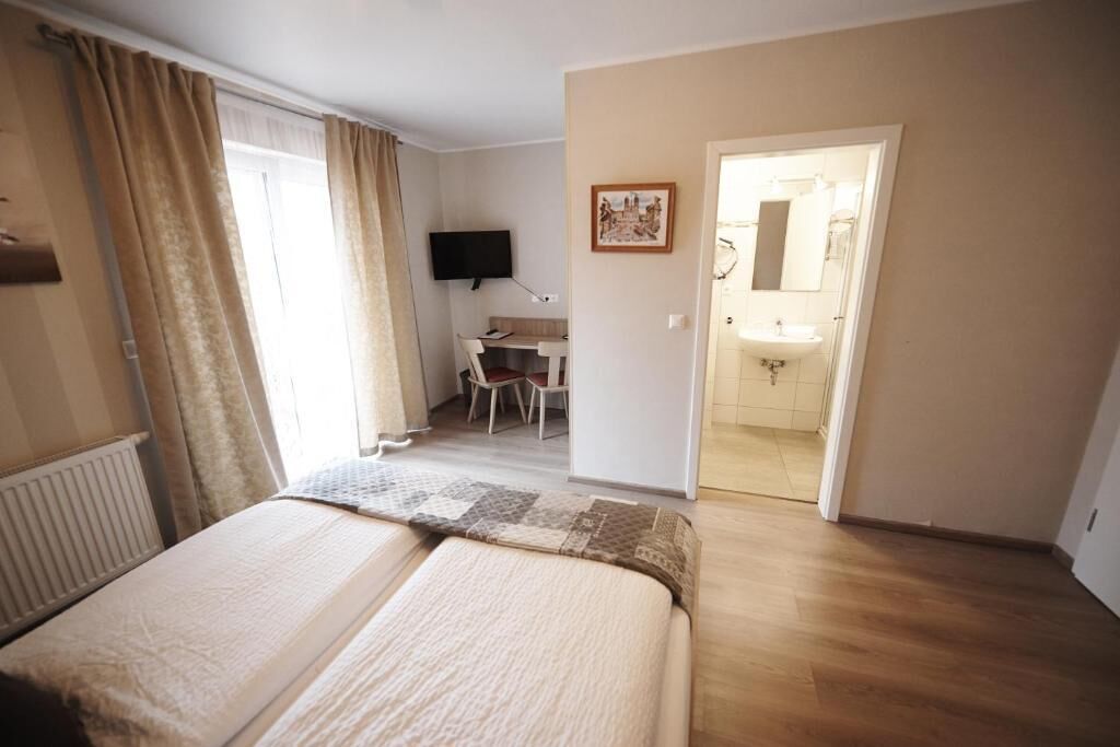 Habitación de hotel con cama, escritorio, silla, televisor y baño con lavabo y espejo.