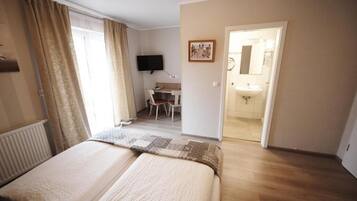 Ein Hotelzimmer mit Bett, Schreibtisch, Stuhl, Fernseher und einem Badezimmer mit Waschbecken und Spiegel.