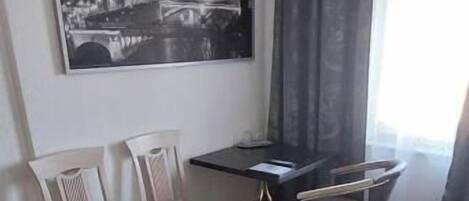 Ett hotellrum med en säng, ett skrivbord, två stolar, en matta och en stor målning med en stadsbild på väggen.