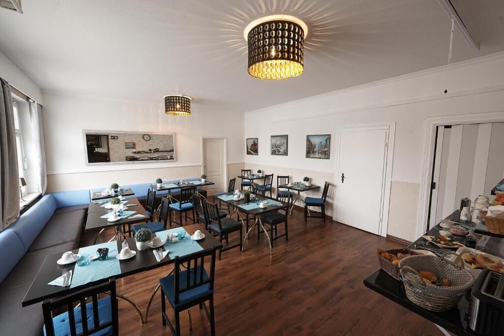 A dining area with multiple tables and chairs, a chandelier, and a view of the kitchen through a window.