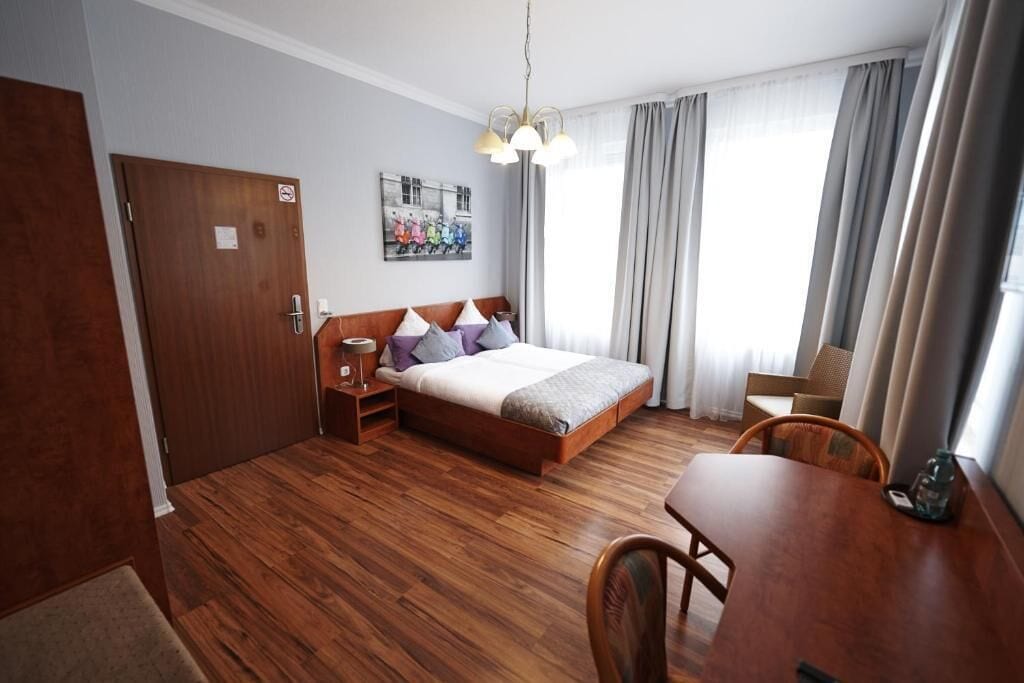 Et hotelværelse med trægulv, seng med puder, et natbord, et bord og en stol.