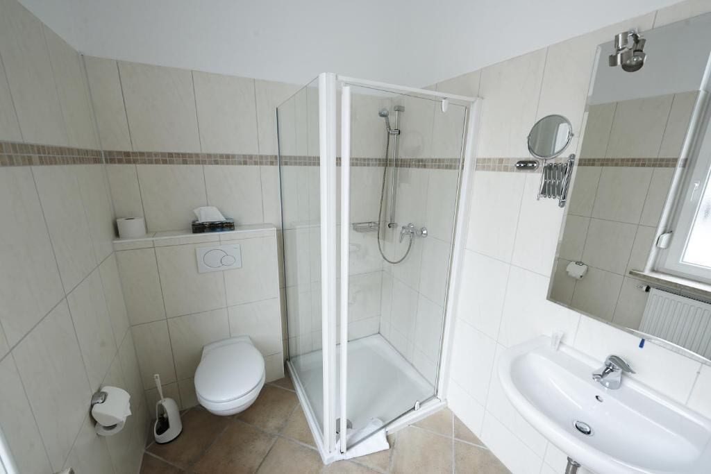 Un baño con ducha envuelta en vidrio, un lavamanos blanco y un inodoro.