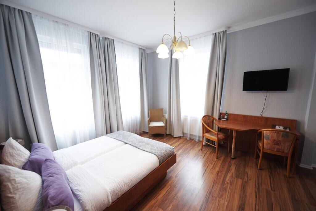 A hotel room with a large bed, a desk, two chairs, a television, and a chandelier.