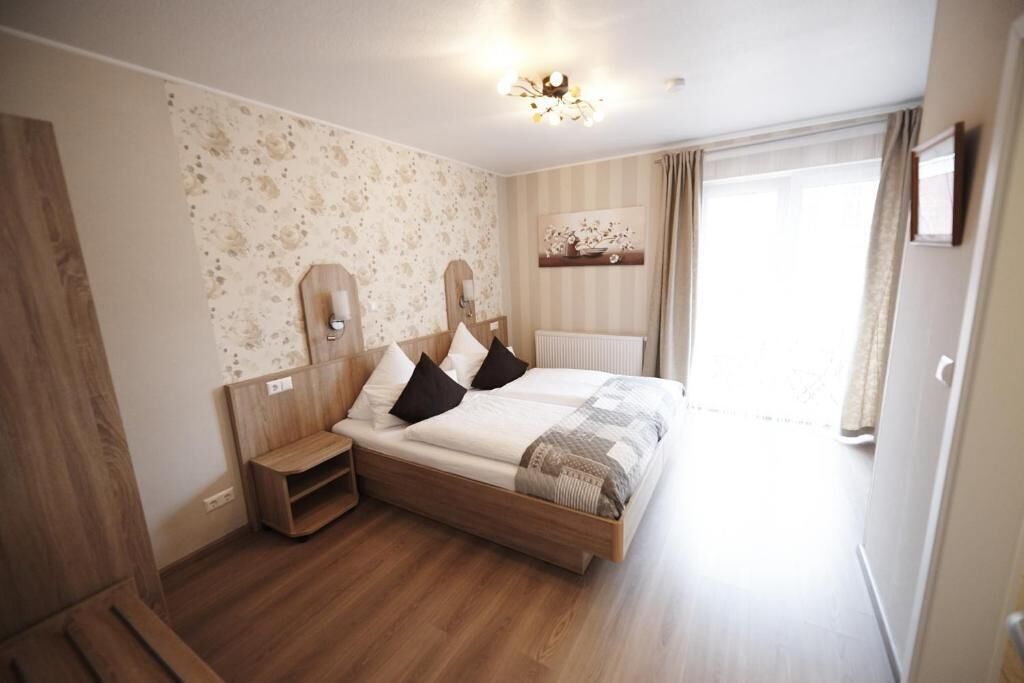 Un dormitorio con cama de madera, mesita de noche, espejo y ventana con cortinas.
