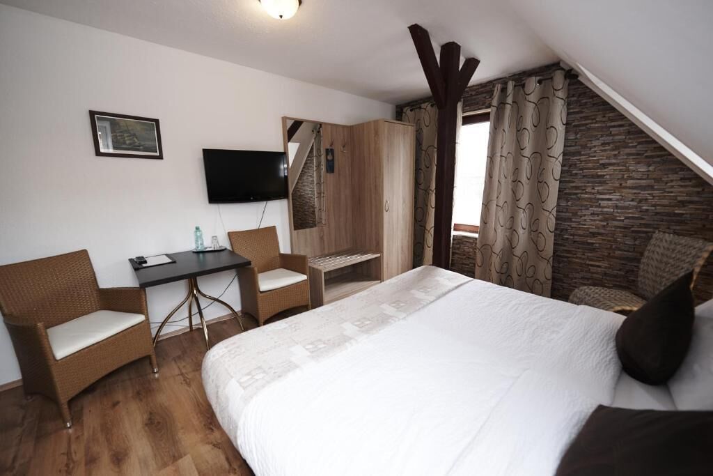 Ein Schlafzimmer mit einem Bett, einem Schreibtisch, zwei Stühlen, einem Fernseher und einer Steinwand.