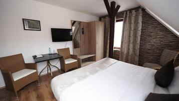A bedroom with a bed, a desk, two chairs, a TV, and a stone wall.