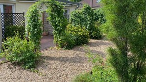 A residential garden with a gravel path, a wooden fence, and various shrubs and trees. - Hotel Wurster Kroog (Bremerhaven)