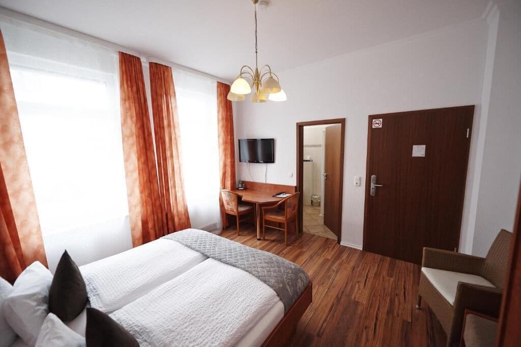 Una habitación de hotel con cama, escritorio, silla, televisor y puerta.
