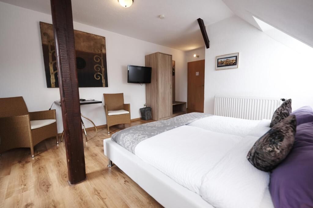 Ein Schlafzimmer mit Bett, Schreibtisch, Sessel, Fernseher und Kleiderschrank.