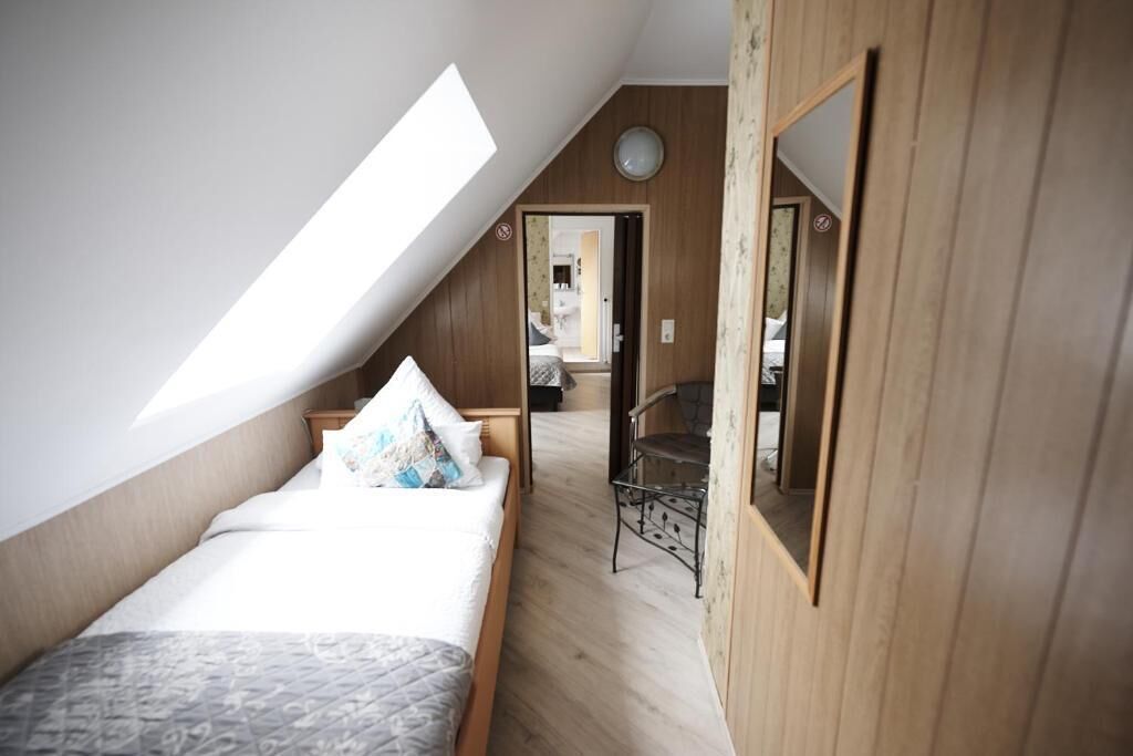 A bedroom with a sloped ceiling, a bed with a patterned bedspread, a wooden wardrobe, and a mirror on the wall.