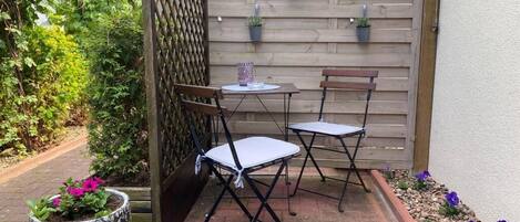A patio area with two folding chairs and a small table, surrounded by a wooden fence and potted plants.