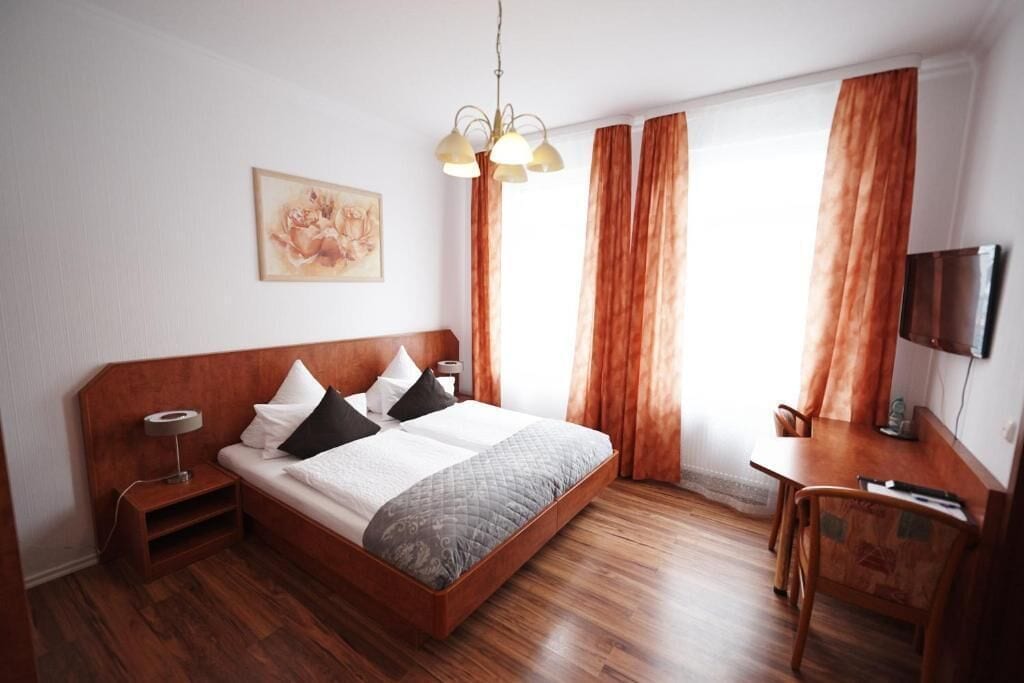 Quarto com cama de madeira, escrivaninha, cadeira, televisão e um quadro na parede.