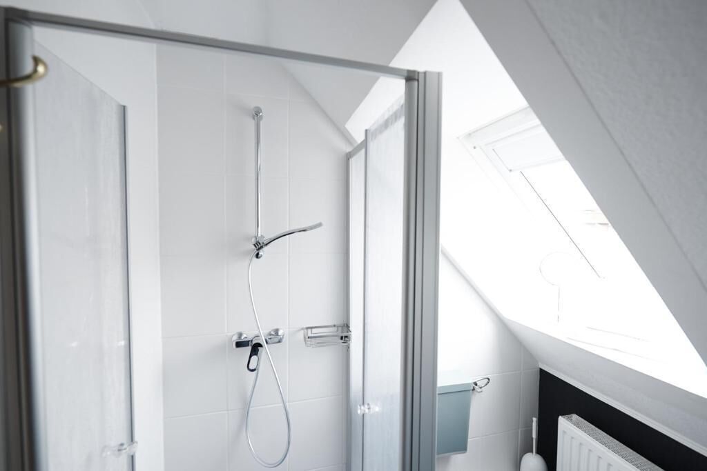 Ducha moderna con puerta de vidrio, cabezal de ducha manual y panel de control en la pared.