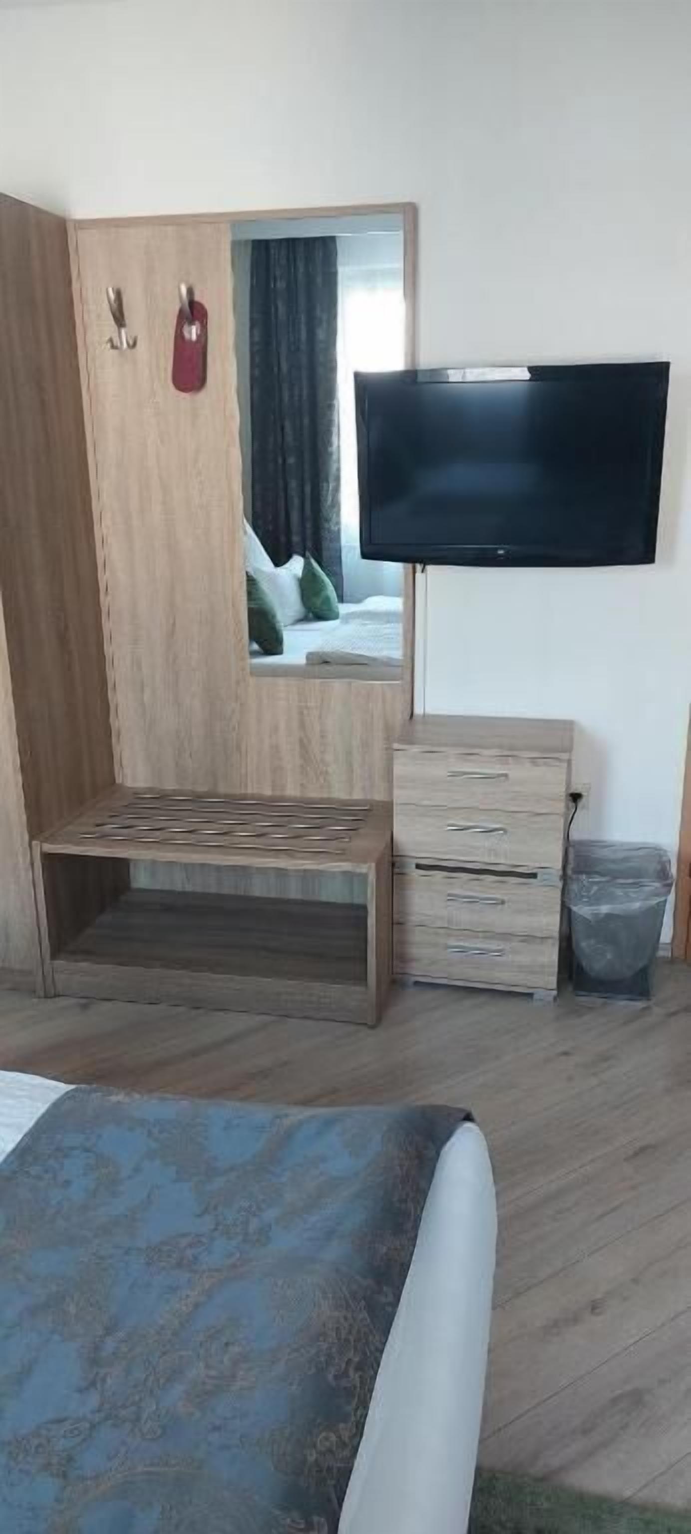 A bedroom with a bed, a wooden wardrobe, a TV, and a small table.