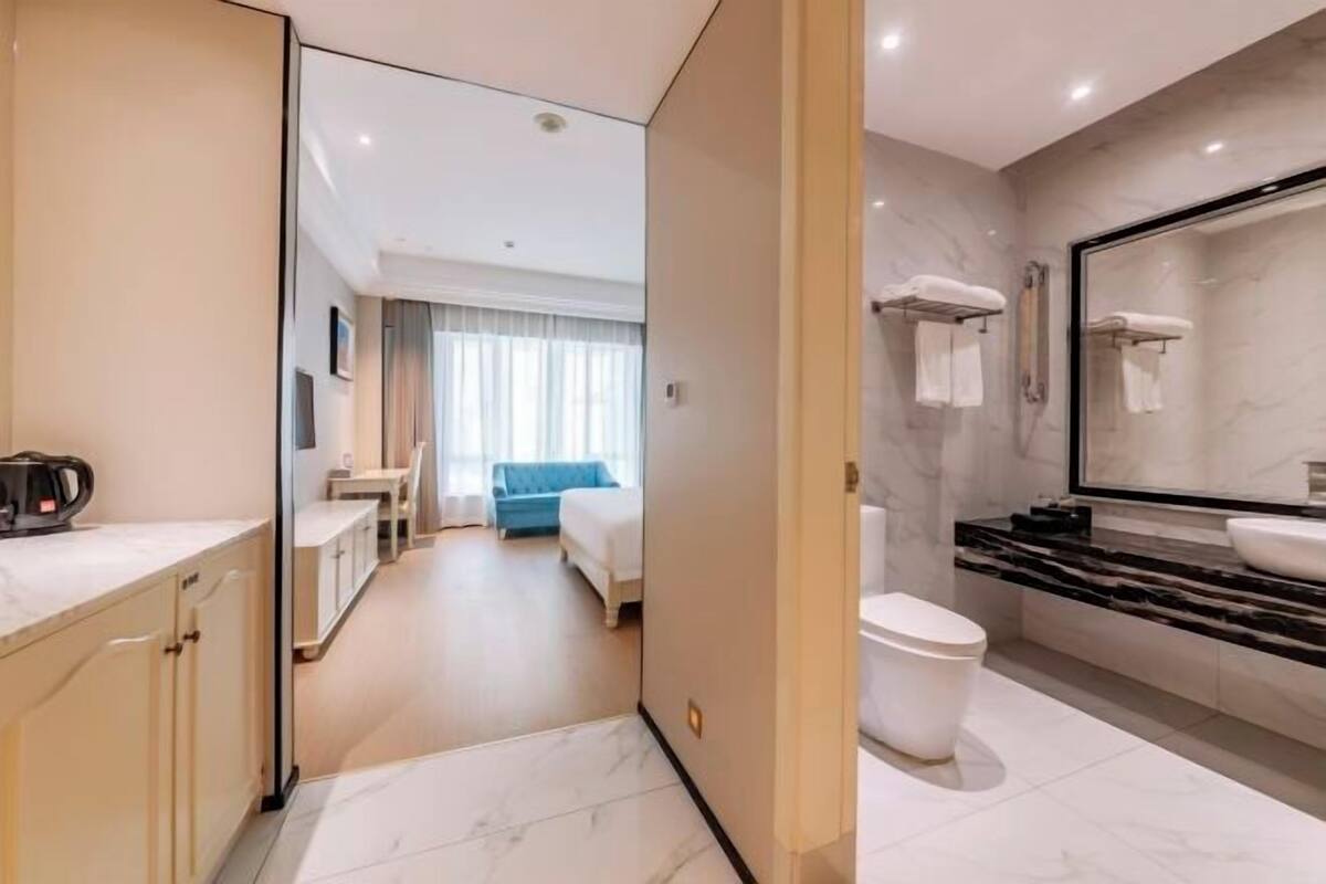 Een moderne hotelkamer met een badkamer, voorzien van een marmeren wastafel, toilet en een grote spiegel.