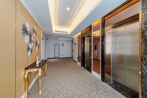Pasillo de hotel con una mesa de recepción, ascensores y suelo estampado.