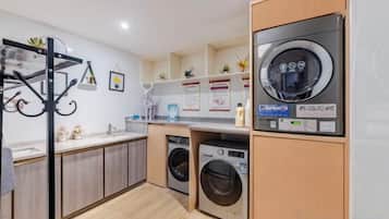 A laundry room with two washing machines, a drying rack, and a shelf with toiletries.