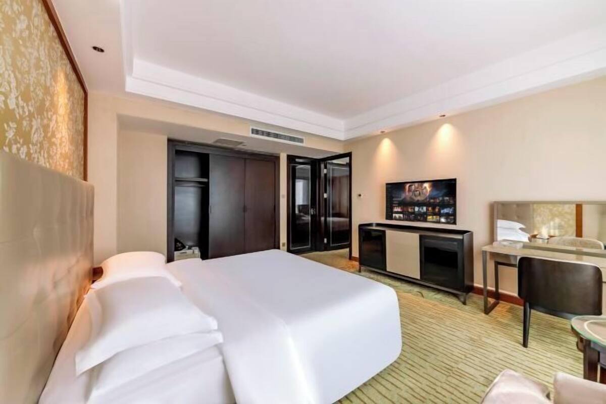 Een hotelkamer met een groot bed, een bureau met stoel, een televisie en een kledingkast.