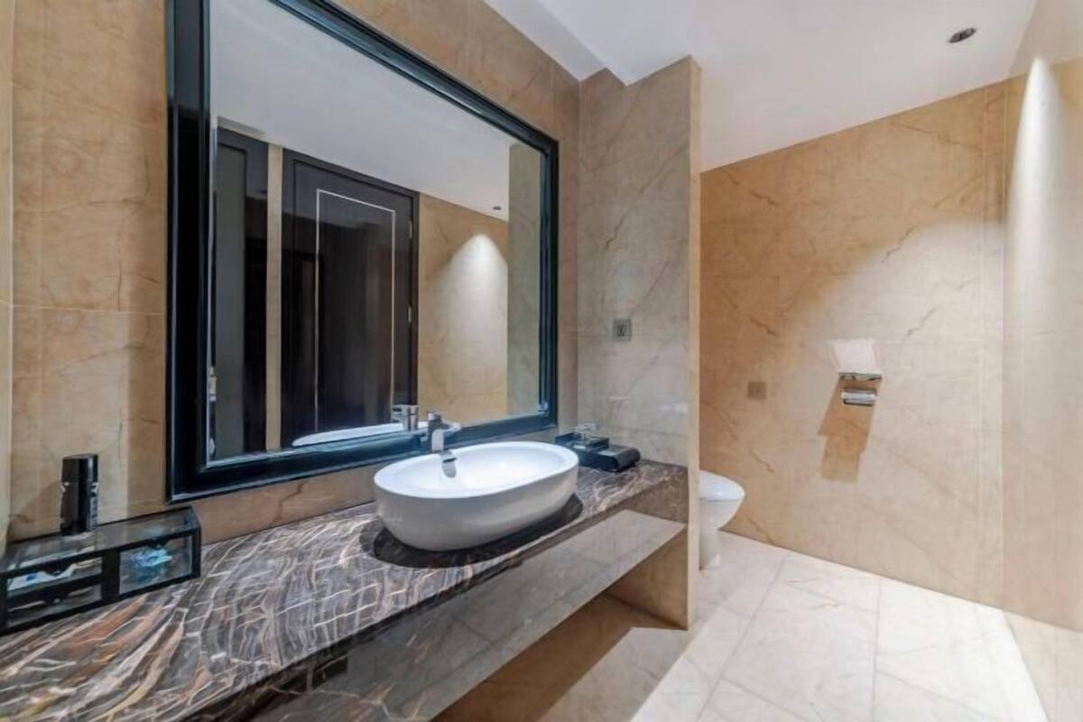 A modern bathroom with a large mirror, a white sink, and a marble countertop.