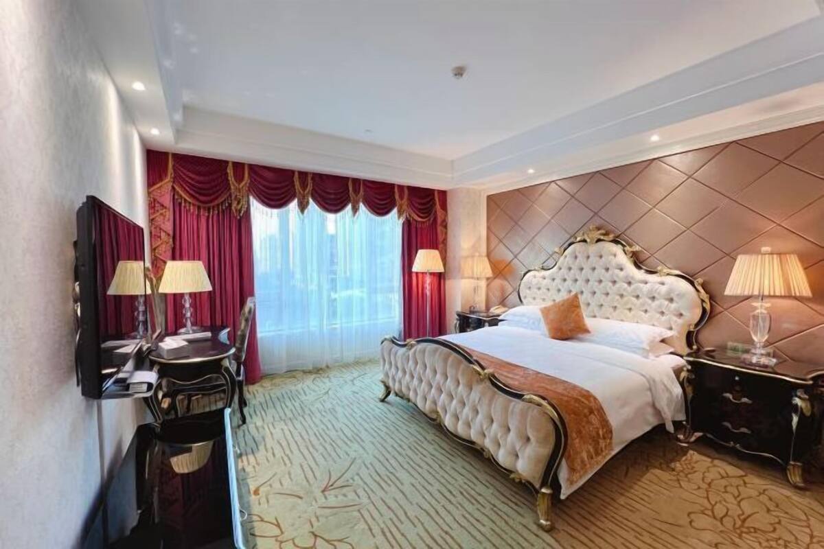 A luxurious hotel room with a large bed, ornate headboard, and elegant decor.