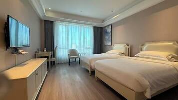 A hotel room with two beds, a desk, a chair, a television, and a window with curtains.