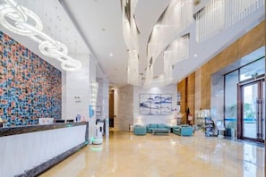 Un vestíbulo de hotel moderno con mostrador de recepción, zona de estar y grandes ventanales.