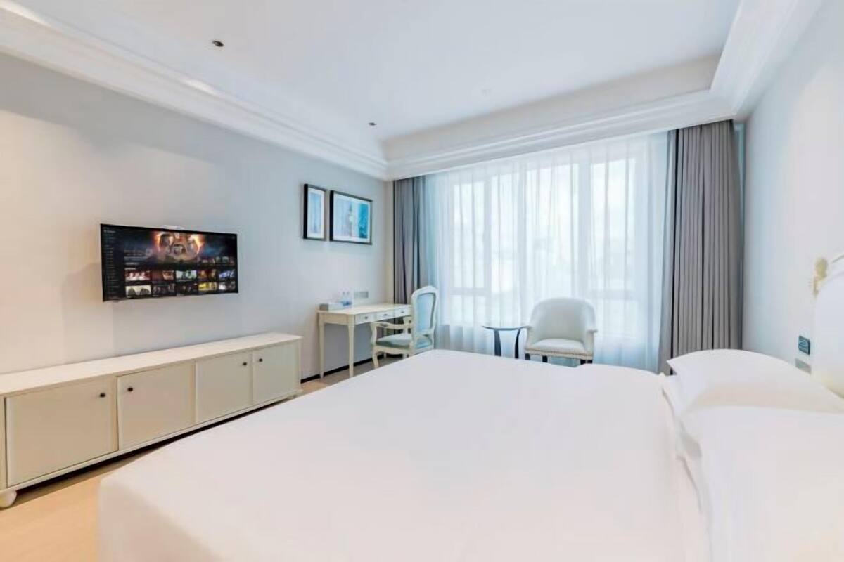 Een hotelkamer met een groot bed, een bureau, een stoel, een televisie en een raam met gordijnen.