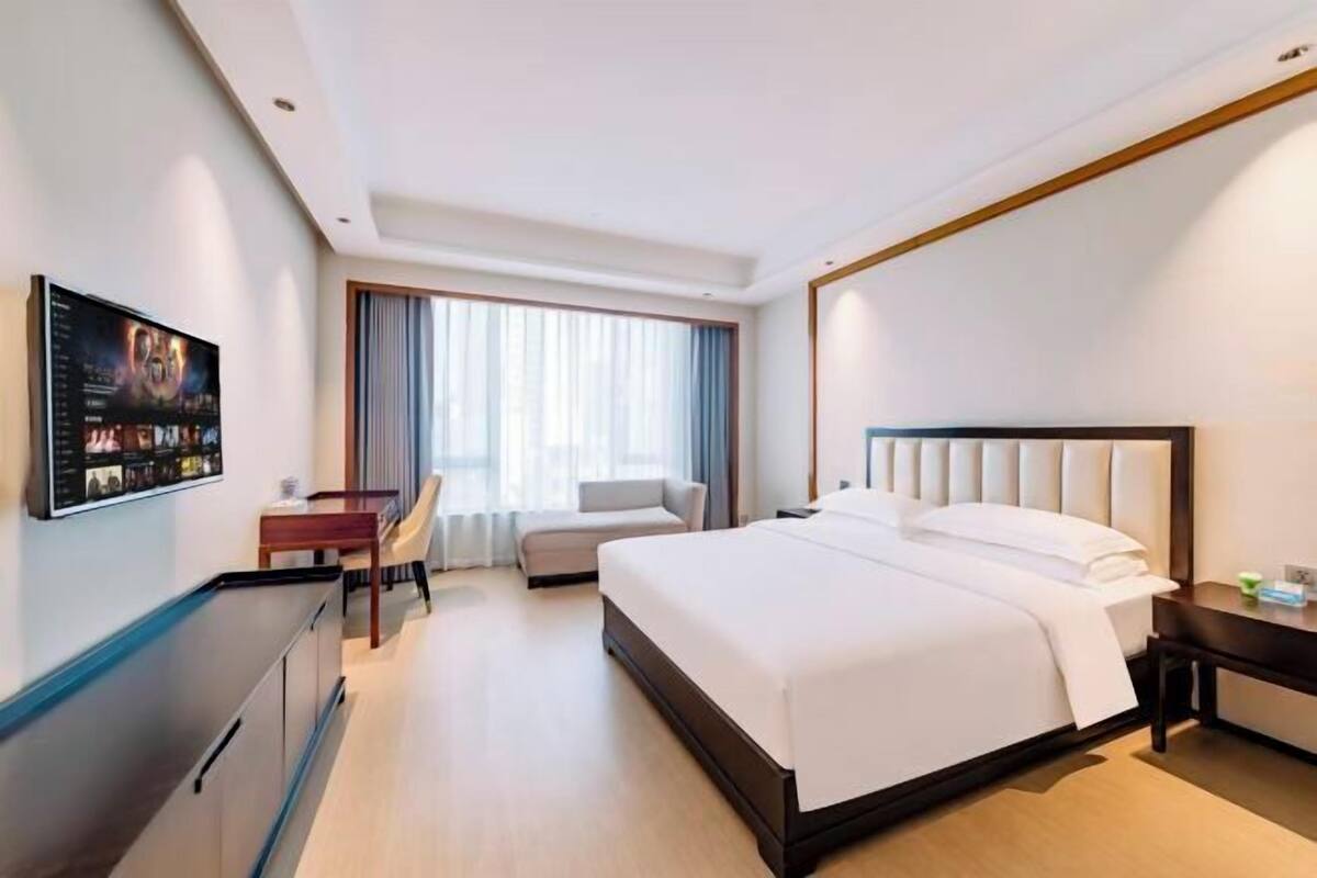 Hotelkamer met een groot bed, een bureau, een stoel, een televisie en een raam met gordijnen.