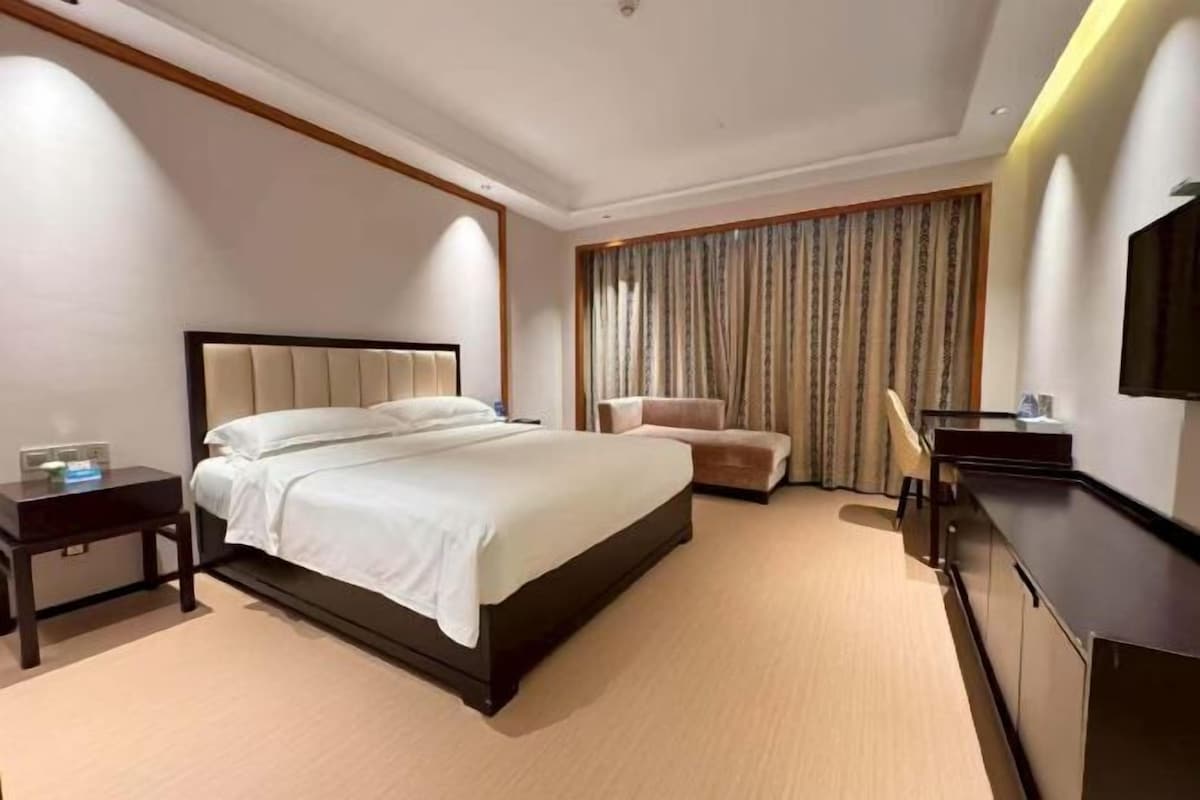 Een hotelkamer met een groot bed, een nachtkastje, een stoel, een bureau en een televisie.