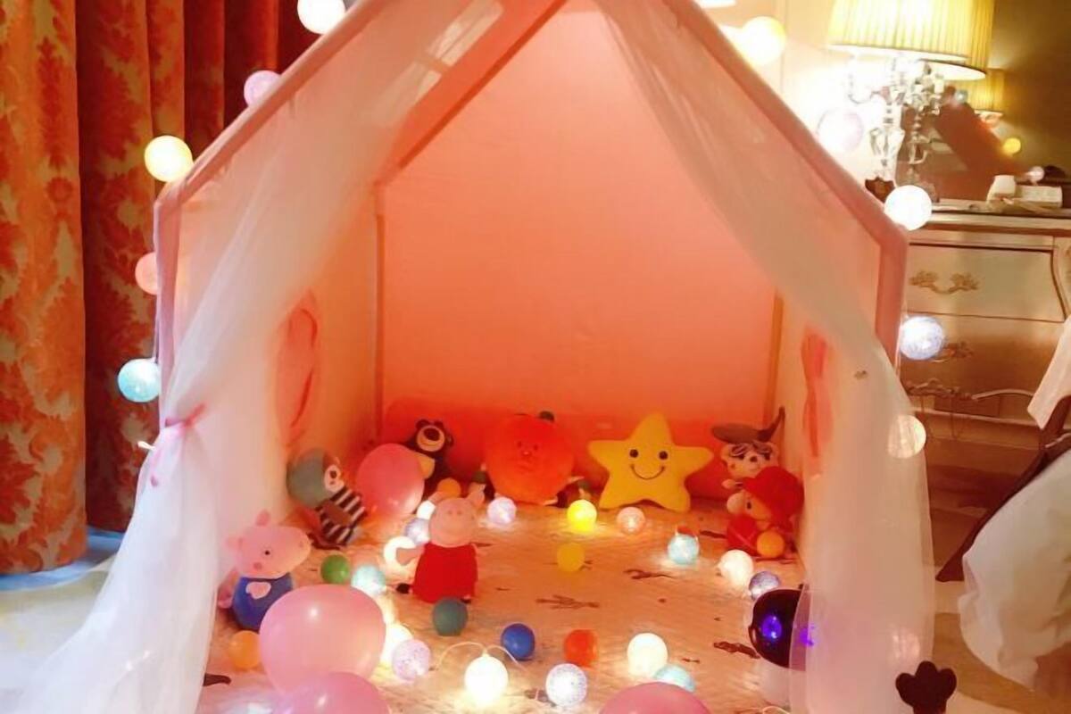 Een gezellige kamer met een tentachtige constructie, versierd met kleurrijke lichtjes en knuffeldiertjes.