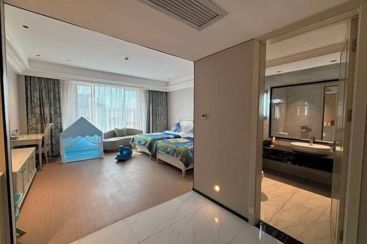 Hotelkamer met een bed, bureau, stoel, een klein speeltentje en een badkamer met wastafel en spiegel.