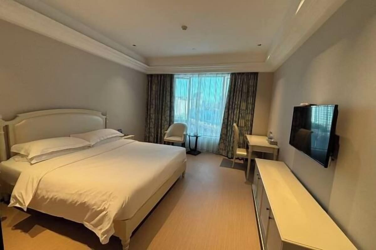 Een hotelkamer met een groot bed, een bureau, een stoel en een televisie aan de muur.