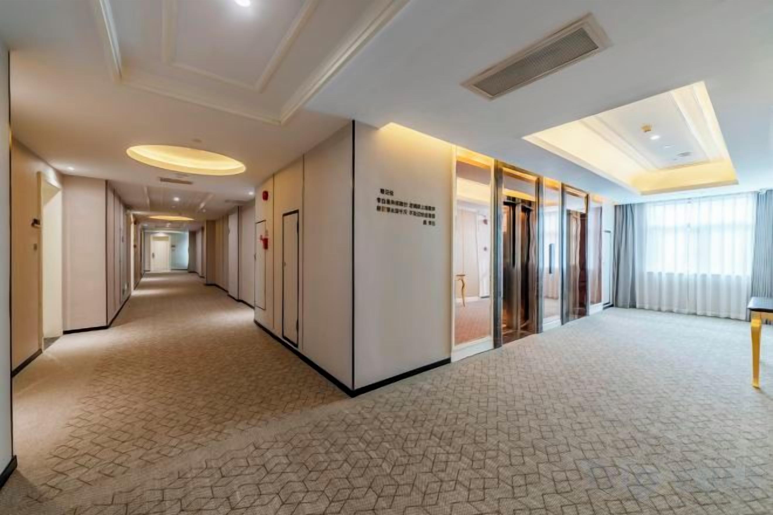 Een hotelgang met een geometrisch patroon in het tapijt, een receptiebalie en een bord met de naam en locatie van het hotel.