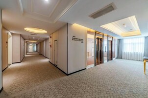 Un pasillo de hotel con alfombra de diseño geométrico, una recepción y un cartel con el nombre y la ubicación del hotel.