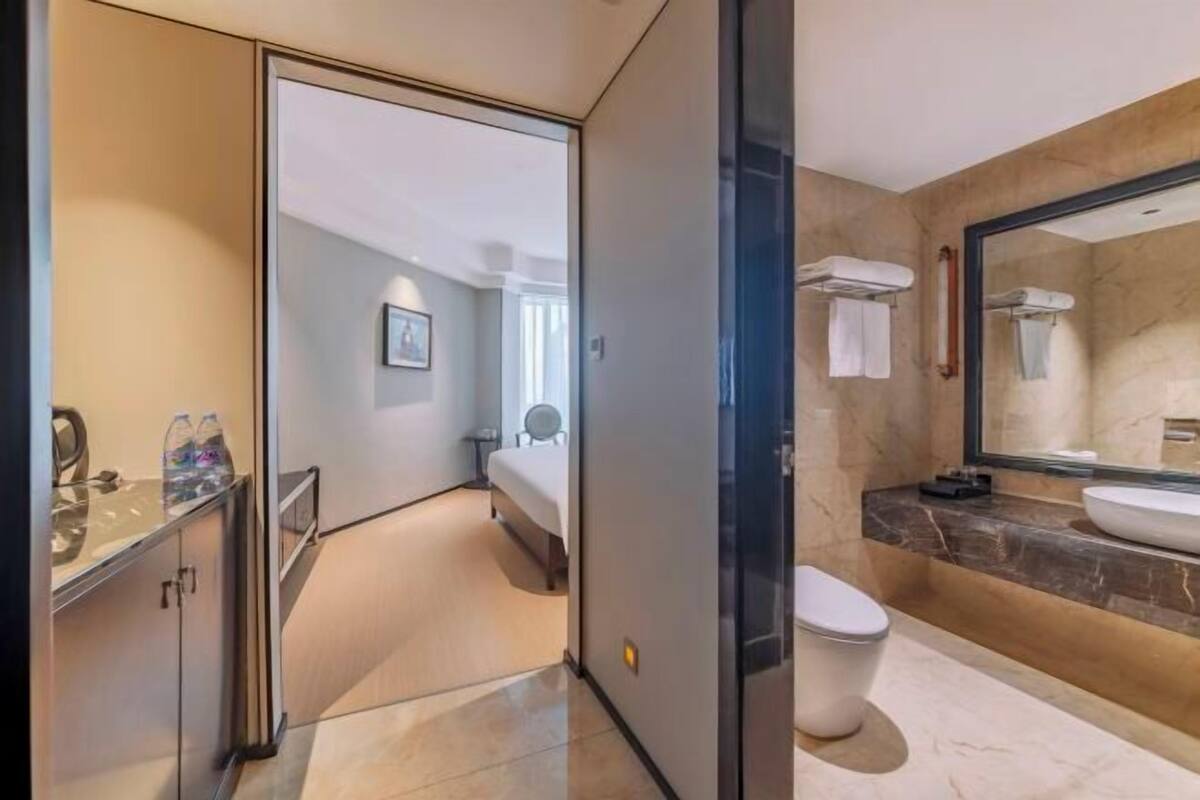 Een hotelkamer met een bed, een badkamer met een grote spiegel, een wastafel en een toilet.