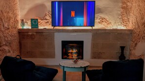 Un salon chaleureux avec une cheminée, un téléviseur à écran plat fixé au-dessus, et deux fauteuils en forme de poire de couleur sombre.