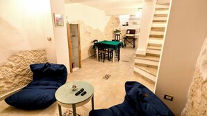 Une pièce confortable avec un lit, une petite table sur laquelle se trouvent un bol et des télécommandes, une table verte avec des chaises, et un escalier menant à un autre niveau.