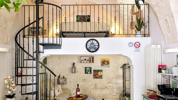 Un coin repas avec une table dressée pour quatre personnes, un escalier en colimaçon et un espace cuisine équipé d’un radiateur et d’une machine à café.