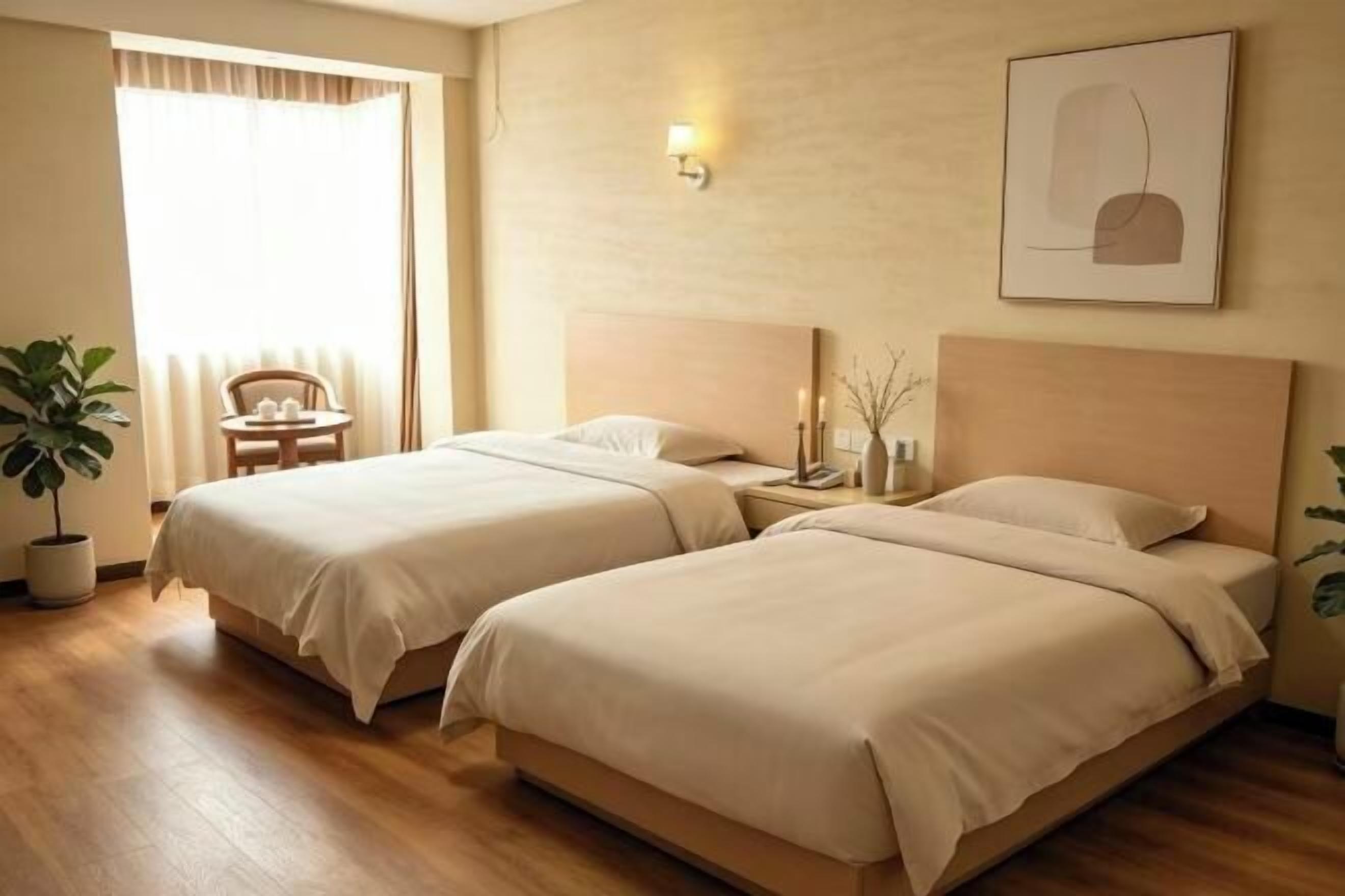 Een hotelkamer met twee bedden, een houten vloer, een kamerplant, een bureau en een stoel.