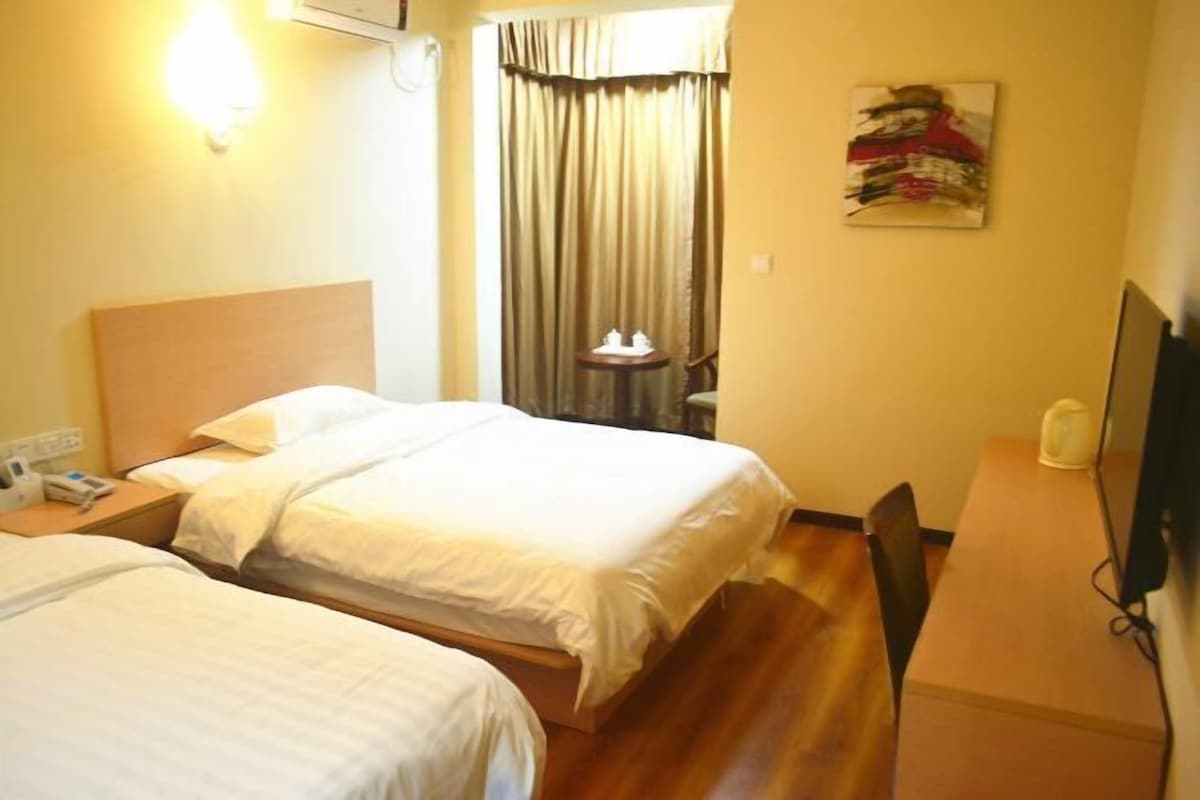 Ein Hotelzimmer mit zwei Betten, einem Schreibtisch, einem Stuhl, einem Fernseher und einem fenster mit Vorhängen.