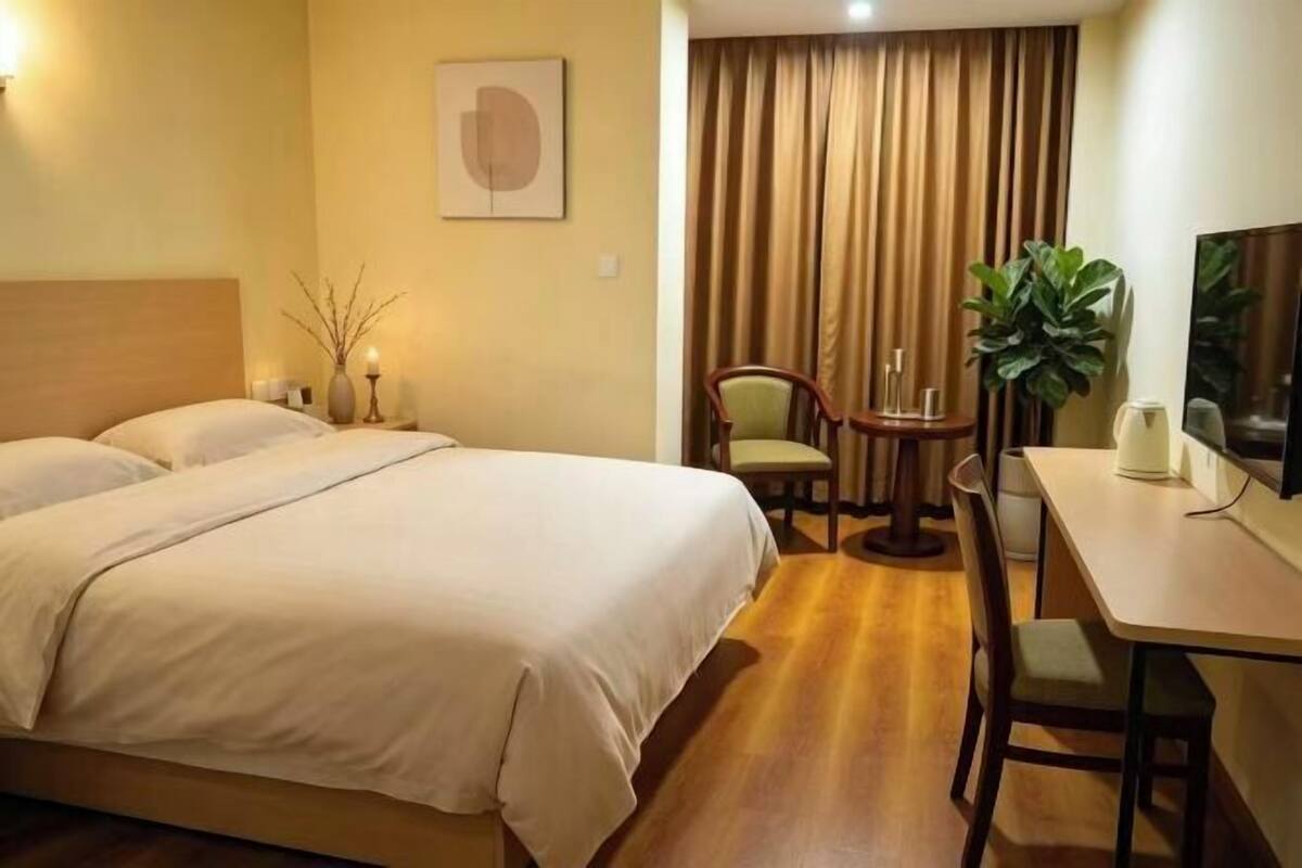 A hotel room with a bed, a desk, a chair, and a plant.