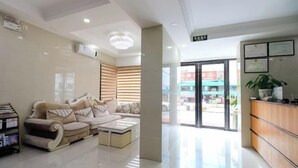 A modern hotel lobby with a sofa, coffee table, and a reception desk. - Haojia Express Hotel (Zhuhai Gongbei Port Fuhuali Branch) (Zhuhai)