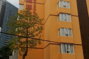 Un immeuble à plusieurs étages, doté d’une façade jaune, de nombreuses fenêtres et d’un arbre bien visible à l’avant.